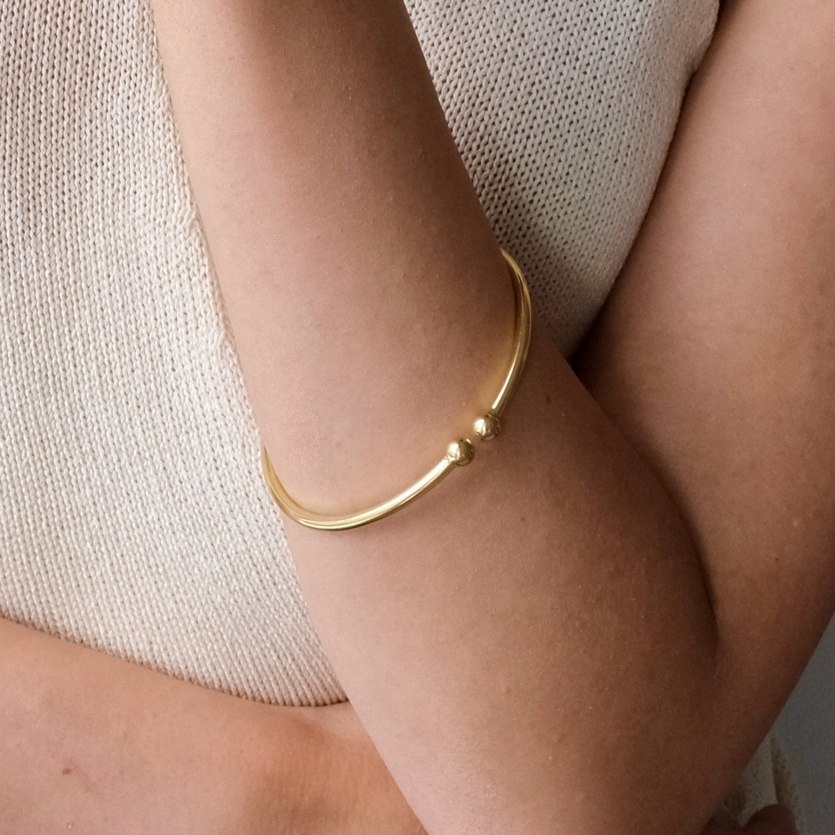 Gold bracelet on a person's wrist with a neutral background