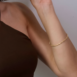 Gold rope bracelet on a person's wrist against a neutral background